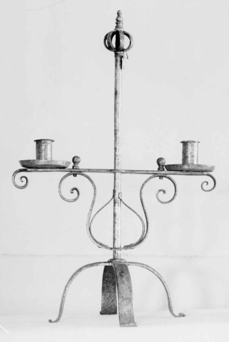 Staken er sammensatt av smidde deler, og består av en firbeint fot med en stang, toppet av en krone. På stangen er en lysarm med to lysholdere. Lysarmen er justerbar i høyden.