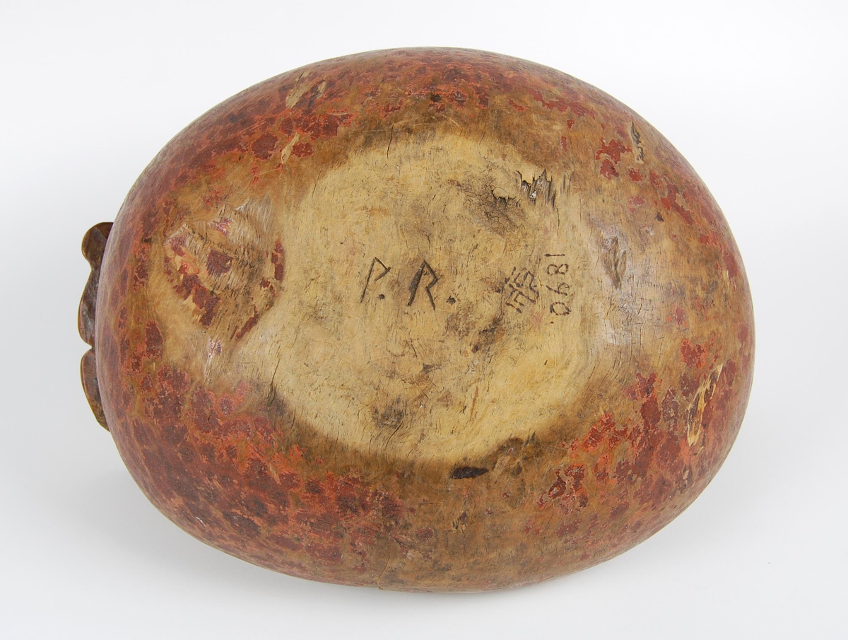 Trøys av bjørk. Oval form. Utskåret mannshode med munnåpning. Håndtak med hakkformete utskjæringer og innskrift. Svarte bekklumper i bunnen.