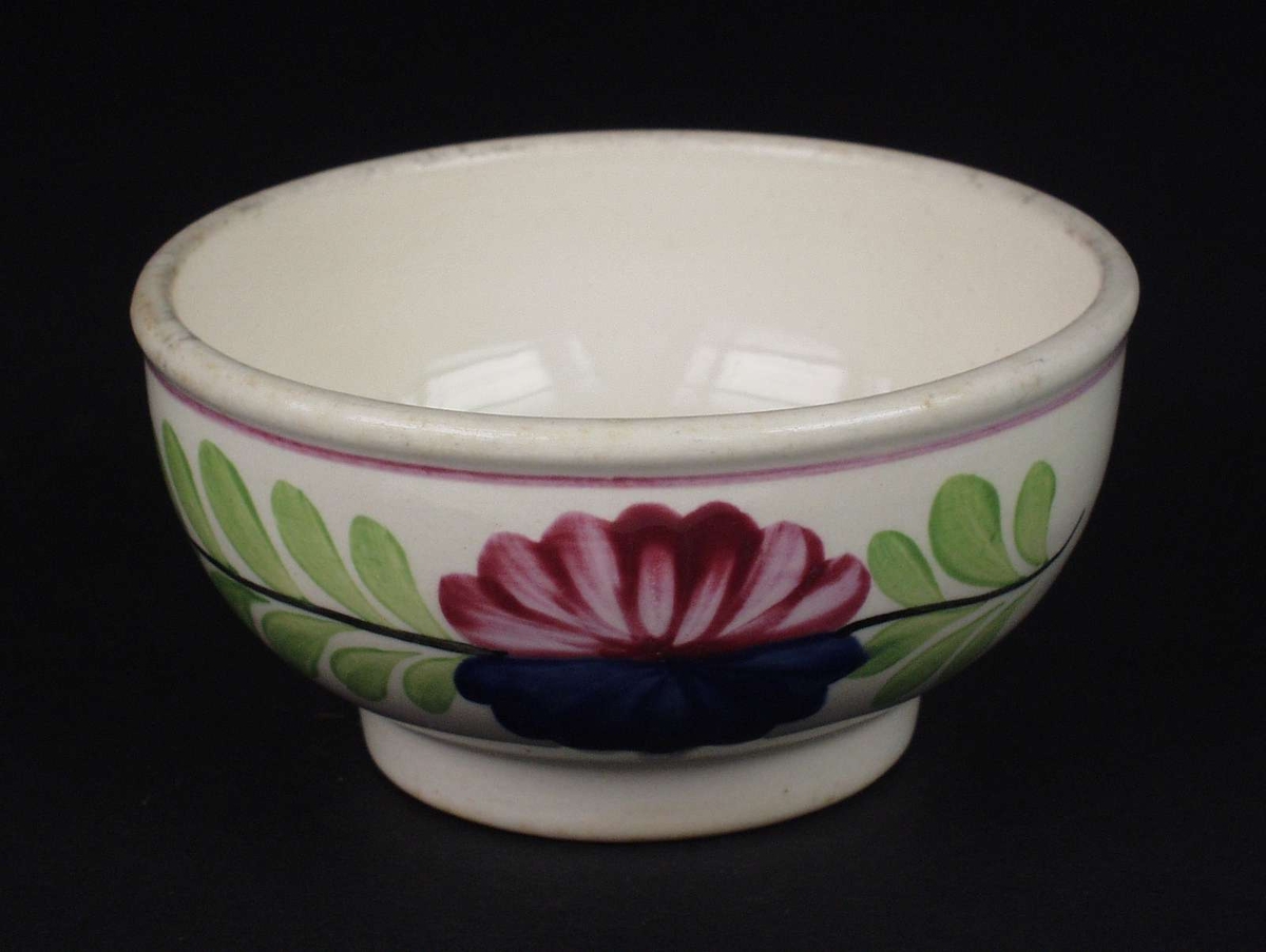 Deler av servise i steintøy og flintgods. Godset er hvitt med malt blomsterdekor. Rød og blå blomst i midten med en ranke av grønne blad.