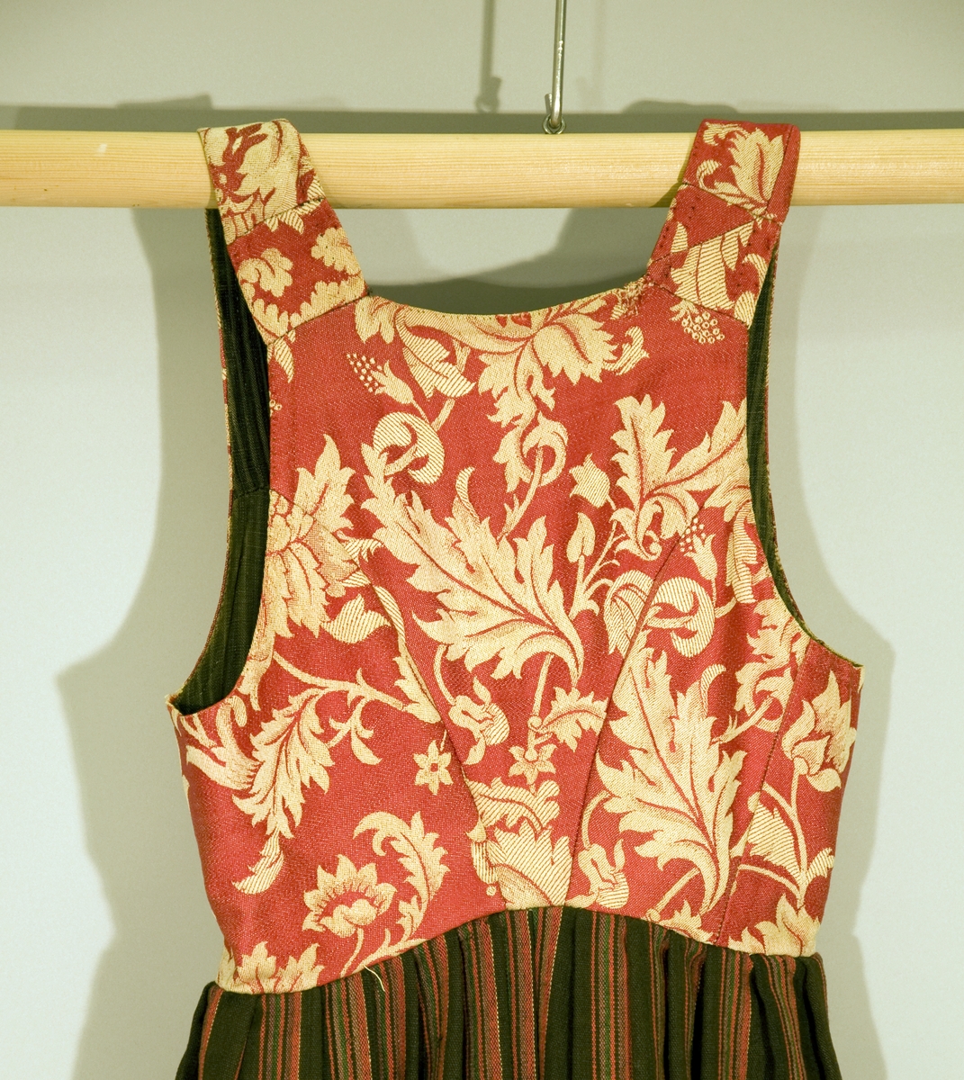 Håndsydd livkjole med stripete ullskjørt og rødt ullliv med store plantemotiv. Livet har rett hals bak, skjøtte seler og mangler ryggsøm. Lukningen består av fire par hekter og tre par hemper til snøring. Åpen klaff.
Fõr av stripete håndvevd ullstoff.
Nederst på skjørtet et børstebånd og skoning av et grindvevd bånd.
Skjørtet har en hengefald.