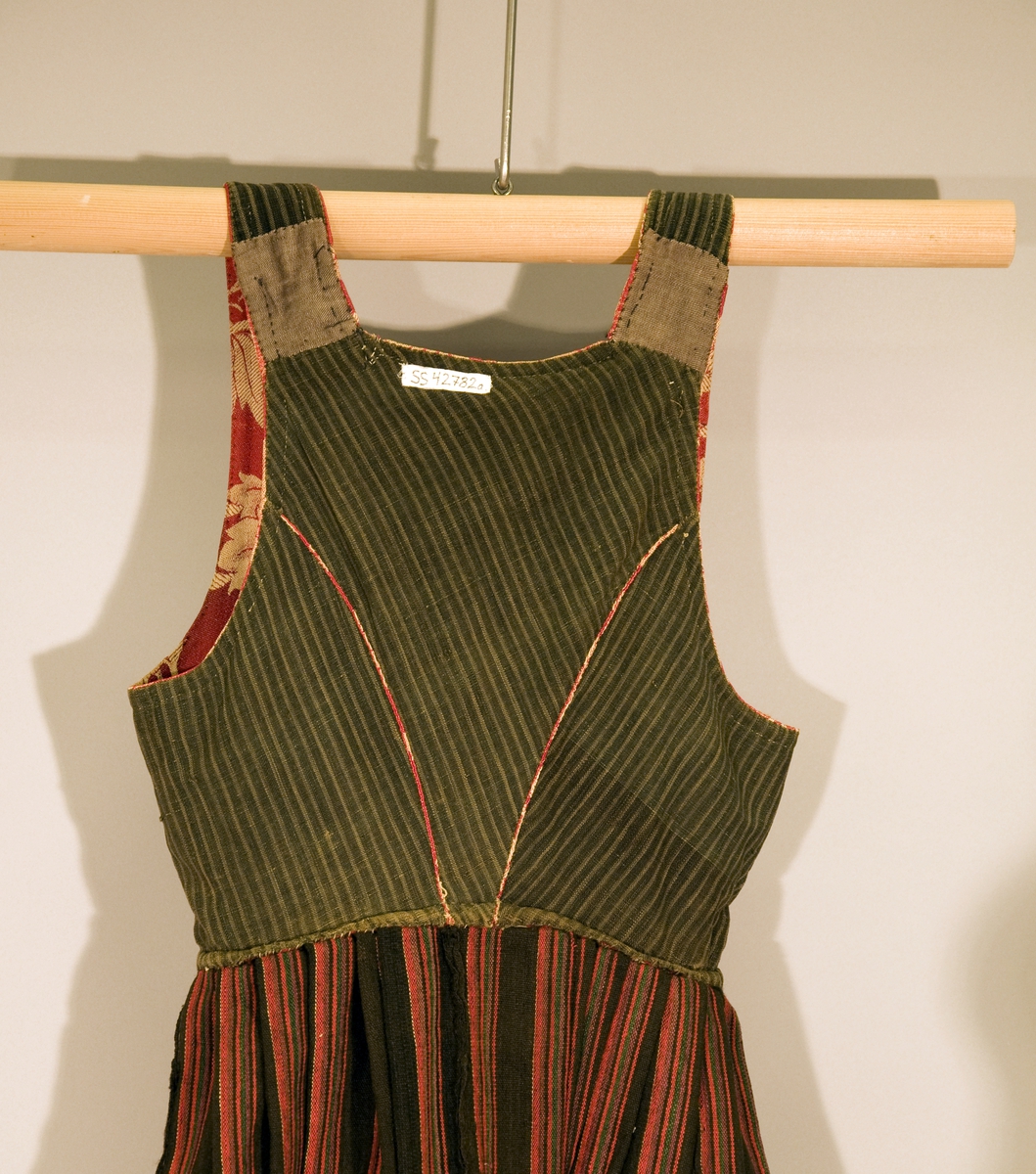 Håndsydd livkjole med stripete ullskjørt og rødt ullliv med store plantemotiv. Livet har rett hals bak, skjøtte seler og mangler ryggsøm. Lukningen består av fire par hekter og tre par hemper til snøring. Åpen klaff.
Fõr av stripete håndvevd ullstoff.
Nederst på skjørtet et børstebånd og skoning av et grindvevd bånd.
Skjørtet har en hengefald.