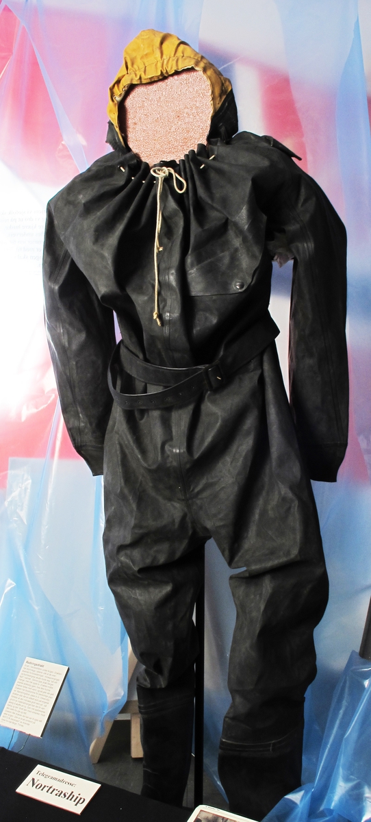 Gummidress, brukt av alliert marine og handelsflåte under krigen 1940 - 45. 
Sort dress med gul hette. Stor gummiddress med påsatte støvler, som har blyinnlegg for å holde drakten flytende loddrett. Lange ermer, vid halsåpning med snoretrekk og gul hette med innvendig hvit elastikk. Innv. bruksanvisning.  Stempel under sålen.