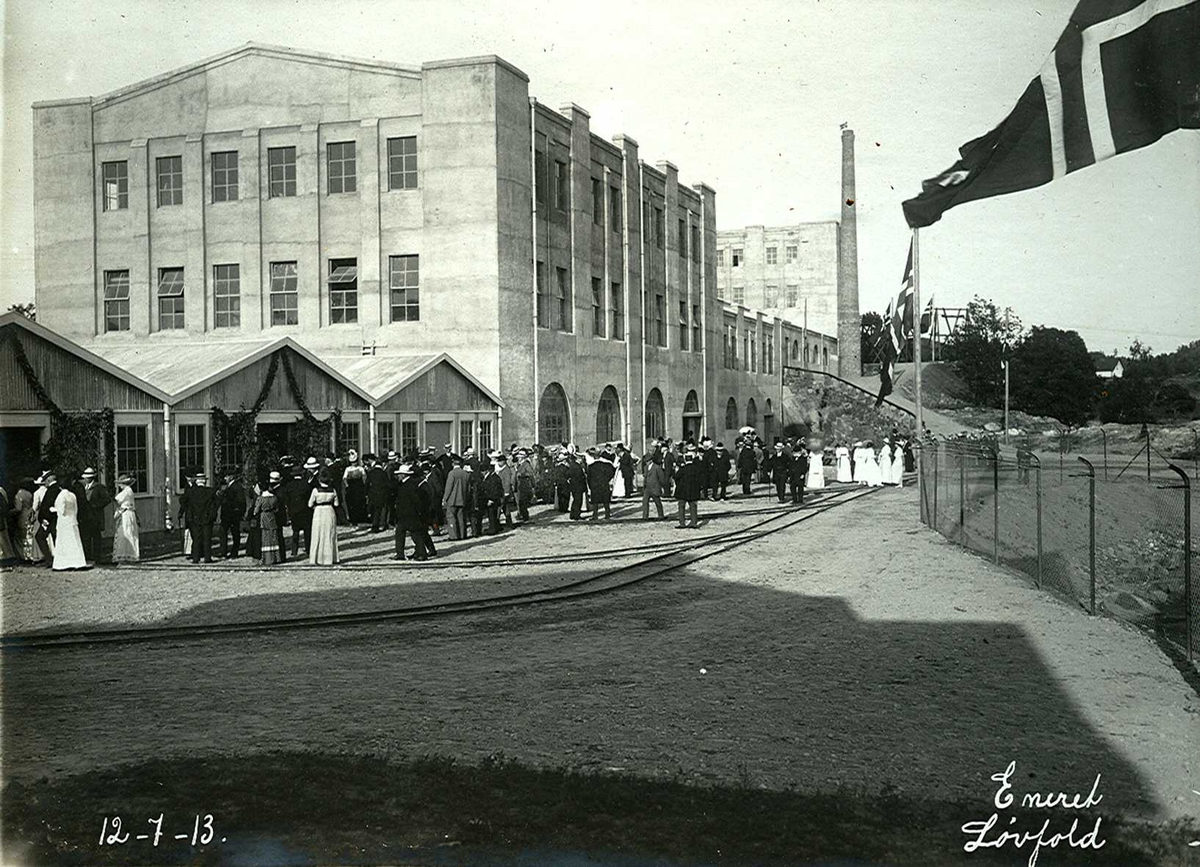 "12/07-1913" Smelteverket. Befaring av fabrikkanleggene i forbindelse med at stedet fikk navnet Eydehavn 12. juli 1913 og offisiell åpning av fabrikken. Det var pyntet med løvkranser og flagg. Etter "dåpsseremonien" ble de besøkende ble vist rundt på det den gang ca. 5000 kvadratmeter store fabrikkanlegget. Bygningene i forgrunnen er Kjemisk vaskeri, og Pakkeri. Murbygningen er Mølle II (finknusing av produktet), deretter Ovnshus II, Rørovnshus med skorstein og Mølle I (grovknusing av råmaterialer).
 
