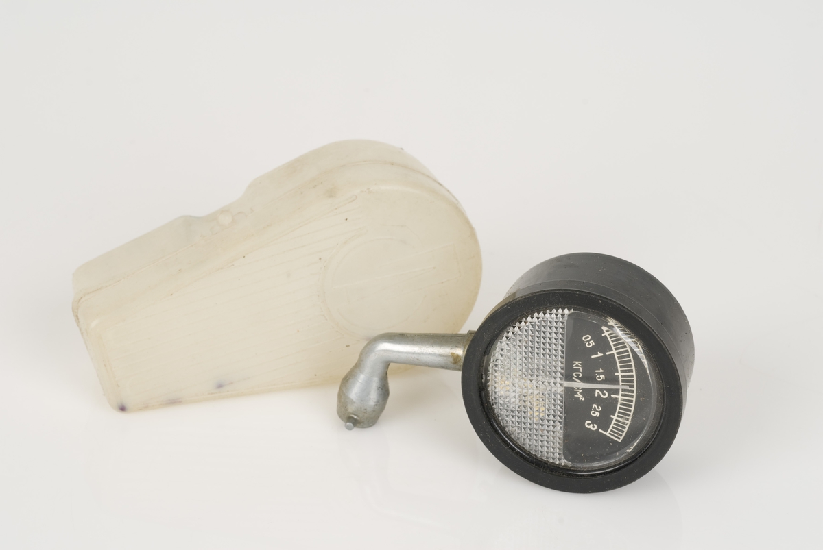 Et manometer (trykkmåler) av metall i en plastboks.
Månometeret er i fargen sort. Skala: 1-3. Produsert i Sovjet.

A: Manometer
B: Etui