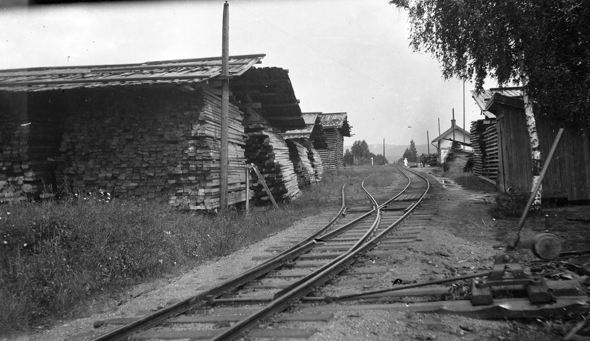 Ved- og plankelagre som venter på transport, trolig under krisen i 1918. Det pågår oppsetting av stolper for elektrisk belysning. Stasjonen har fremdeles utvendig parafinbelysning.