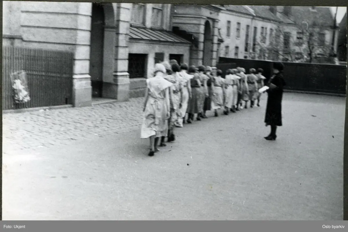 Jenter på rekke og rad holder mannekeng-oppvisning i skolegården. Albumtittel: "Sofienberg skole femti år - første september 1933."