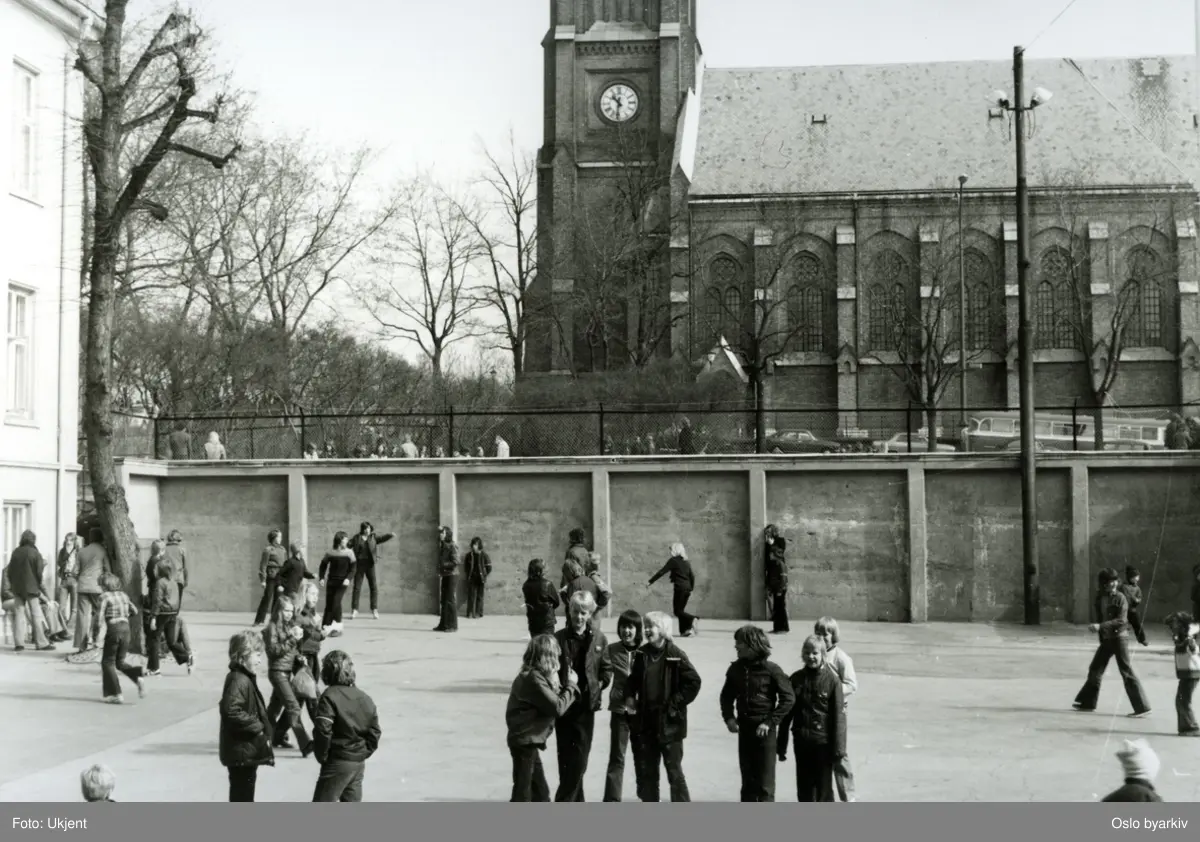 Elever i skolegården på Uranienborg skole. Bildet tatt i forbindelse med "Aksjon Spire 1973" på Uranienborg skole på området mellom Harelabbveien, Briskebyveien og Skovveien (lokalnavn "Harelabben" etter planten harelabb). Uranienborg kirke i bakgrunnen.