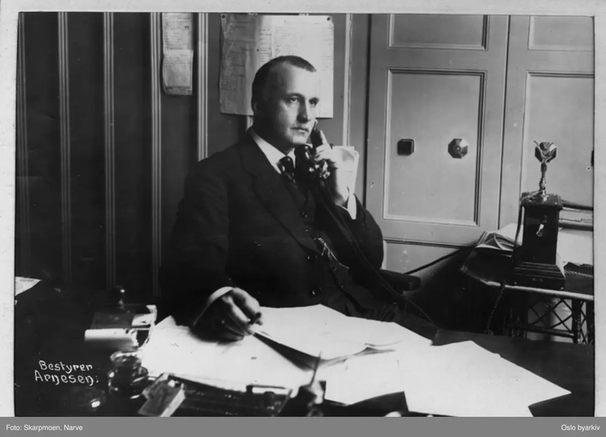 Mann ved skrivebord, sitter i telefonen.