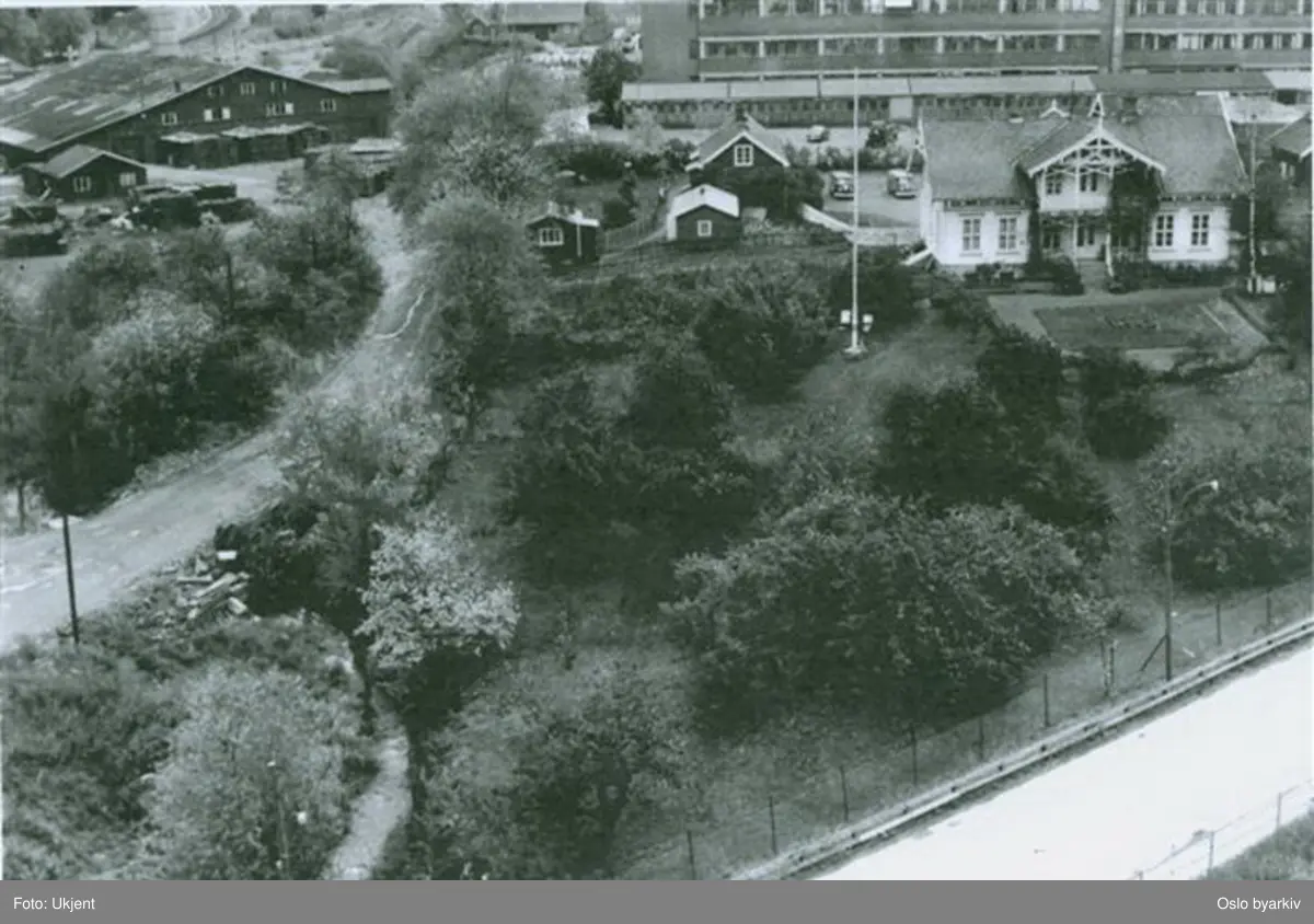 Hovedhuset på Mellom Hovin (revet 1997) og bygninger på STK i bakgrunnen. Daværende Østre Aker vei i bru over Hovinbekken, som fortsatt går åpen i forgrunnen. Bak ligger Akers teglverk (revet 1988). T-banens trasee sees så vidt i øvre bildekant. Bildet er tatt 1967 fra høyhuset i Ulvenveien 88.