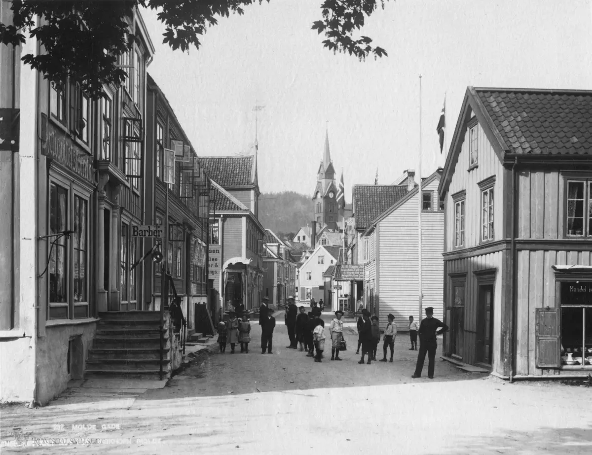 Storgata sett østover, Antikvitetshandler Ulrik Weinholdts butikk til venstre..Molde med kirken i bakgrunnen. .Lenger opp i gaten til høyre: A.S Hagen, gullsmed..Ludvig Hansen sin butikk til venstre oppe i gata..Brennevinsutsalget hus nr 2 på høyre side..Muligens er bildet fra ca 1910 da det hverken er eletrisk gatelys eller parafin gatelys i gatene. .