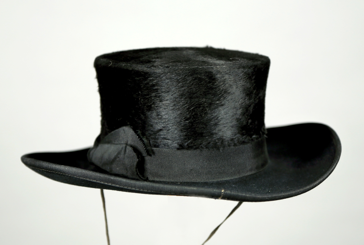 Hatt av filt og felpel med ribbet bånd rundt pullen, og bomullsbånd til ¨ha under haken. 