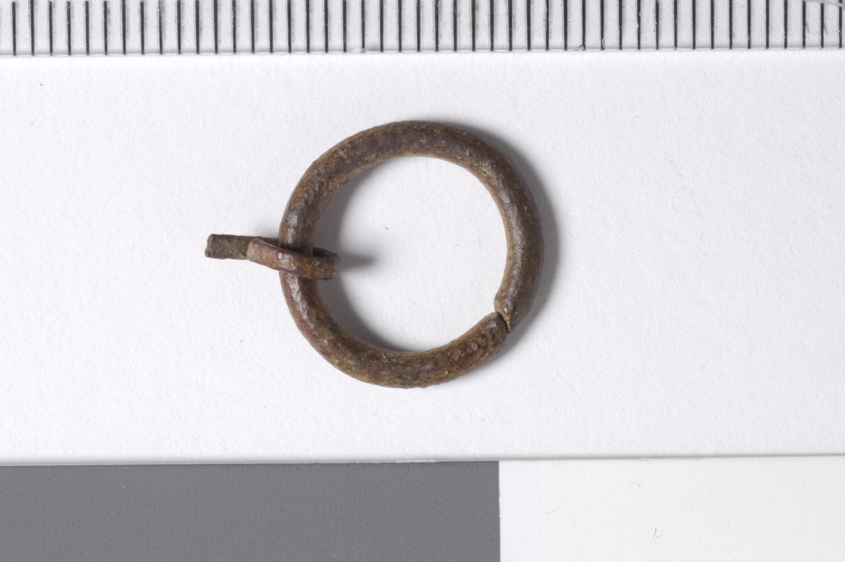 MALV: DIAM. 14, 2  T. 2 MM, ÅPEN RING UTEN DEKOR. TORNEN ER LAGET AV 1, 5 MMMETALLBÅND, DEN ER BRUKKET. 