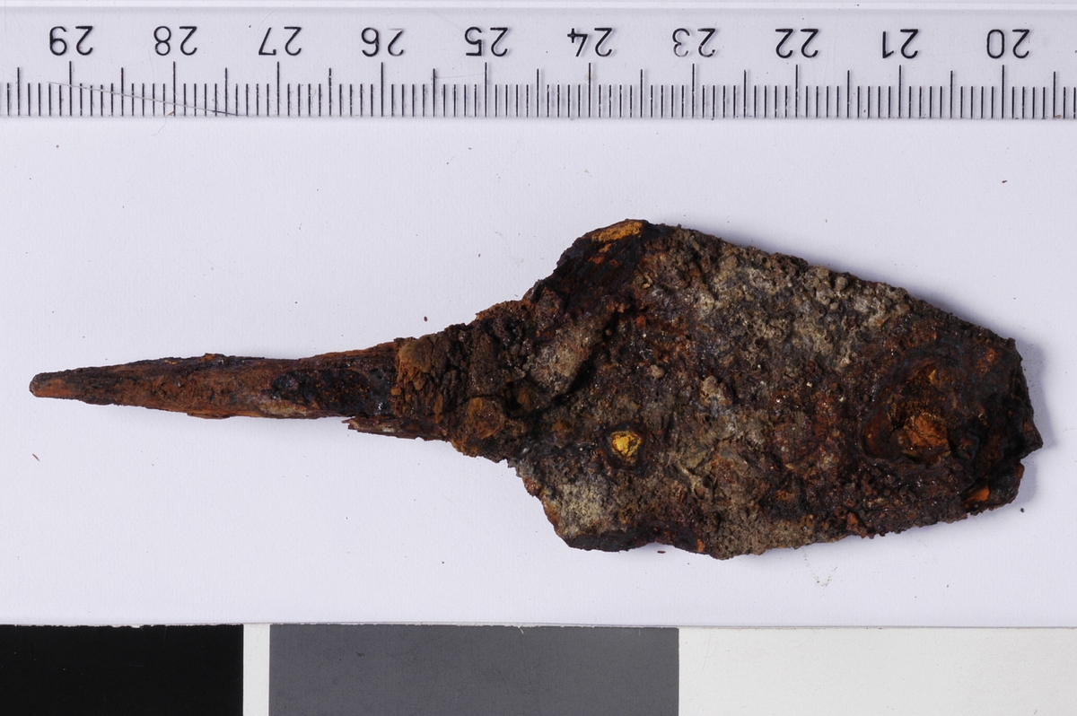 MÅL: L. 112 MM B. 32 MM, BLADFORMET SPISS MED TANGE. INGEN TYDELIG MIDTRYGG. SPOR AV TREVERK VED ROTEN AV BLADET (TILNÆRMET RYGH 547). Spissen brukket.