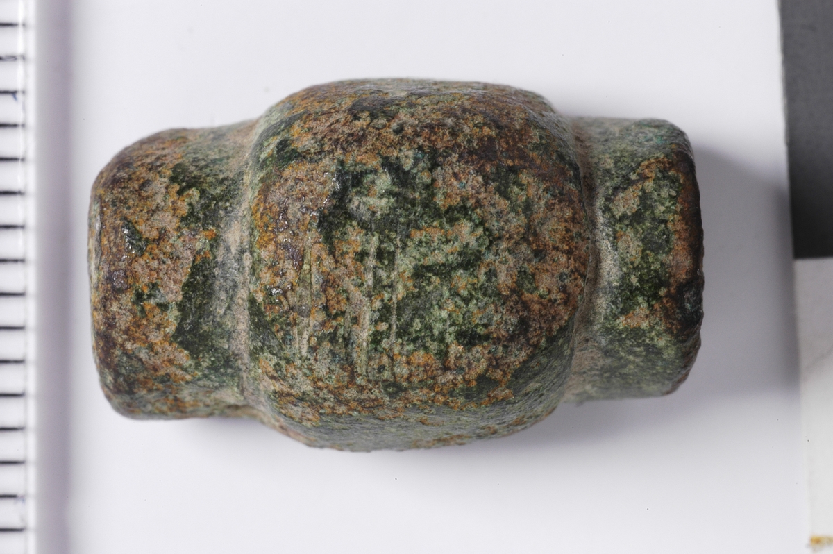 Avlang metallgjenstand med tilnærme halvkuleformet tverrsnitt. Det midtre partiet er forstørret på alle tre sider, mens gjenstanden er flat i bunnen. I endene sees rester av bruddflater i nede halvdel av kantene. Gjenstanden kan være en del av ei rett draktspenne som har vært noe lengre.