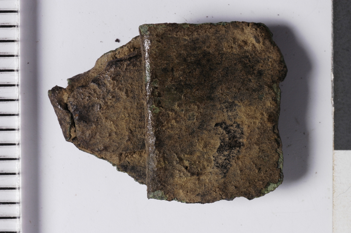 MÅL: L. 1, 6 CM B. 1, 3 CM, TYNN BRONSEPLATE, UREGELMESSIG FASONG. SAMMENBRETTET. GJENNOMGÅENDE FLATHAMRET NAGLE.