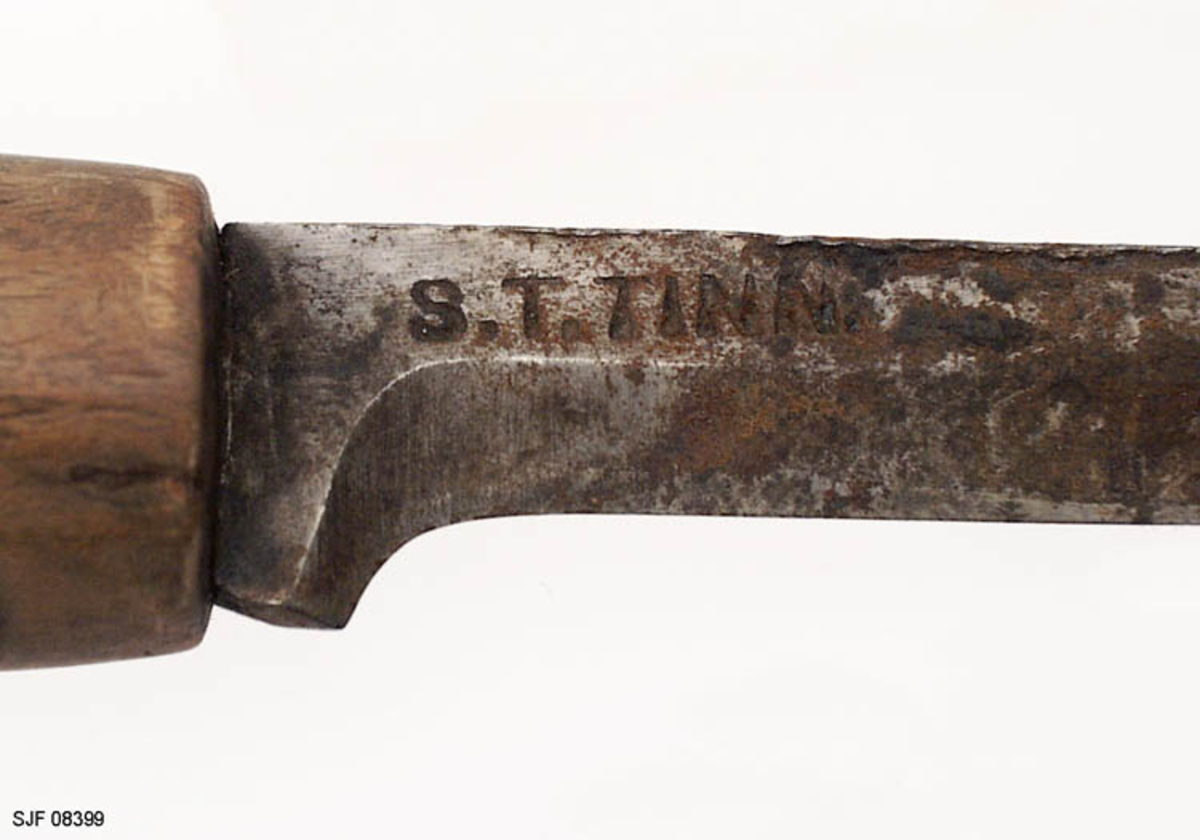 Tollekniv uten slire, lagd av smeden Svein Svimbil (1888-1987) fra Tinn Austbygd i Vest-Telemark. Kniven er 19,5 centimeter lang. Knivbladet utgjør 9,1 centimeter av dette lengdemålet. Bladet er 2,1 centimeter bredt bakerst ved brystningen, men egglinja er slipt såpass mange ganger at bladbredden på midten er bare om lag 1,5 centimeter. Bladtjukkelsen er om lag 4 millimeter ved brystningen, men bladet tynnes gradvis framover mot knivspissen. Bladryggen er forholdsvis rett, riktignok en aning konvekst buet i den fremre enden, der sidekantene er avfasete. Smeden har plassert stempelet sitt - «S.T. TINN» bakerst på det som når kniven holdes i arbeidsstilling er høyre bladside. De nevnte initialene refererer til Svein Tverberg, som var det navnet smeden brukte før han kjøpte småbruket Svimbil.