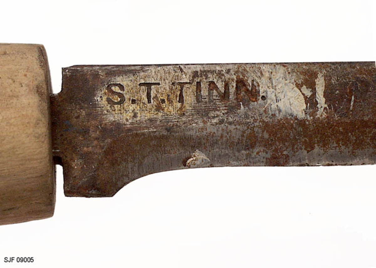 Tollekniv uten slire, lagd og brukt av smeden Svein Svimbil (1888-1987) fra Tinn Austbygd i Vest-Telemark. Kniven er 18,5 centimeter lang. Knivbladet utgjør 8,6 centimeter av dette lengdemålet. Bladet er snaut 2,0 centimeter bredt bakerst ved brystningen, men egglinja er slipt såpass mange ganger at bladbredden på midten er bare drøyt 1,5 centimeter. Bladtjukkelsen er om lag 4 millimeter ved brystningen, men bladet tynnes gradvis framover mot knivspissen. Bladryggen er forholdsvis rett, riktignok en aning nedoverskrådd i den fremre enden, der sidekantene er avfasete. Smeden har plassert stempelet sitt - «S.T. TINN» bakerst på det som når kniven holdes i arbeidsstilling er høyre bladside. De nevnte initialene refererer til Svein Tverberg, som var det navnet smeden brukte før han kjøpte småbruket Svimbil.