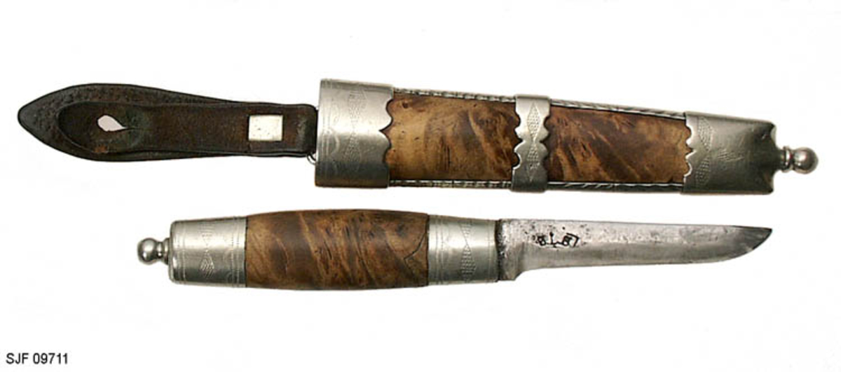 Tollekniv med slire.  Slira er signer "T. B. ", som skal være initialene til Trygve Brenna fra Åmot på Modum.  Bladet er 8, 2 centimeter langt og 1, 9 centimeter bredt ved brystinga.  På den bakre delen av nakken, som er om lag 0, 5 centimeter bred, er det filt to tverrstreker og et kryss.  Høyre bladside har tre innstemplete initialer, antakelig "Ø. L. S. ", innskrevet i ei buet ramme.  Denne signaturen ble brukt av eggsmeden Knut Knutsen Øyo (1860-1921), og seinere av firmaet til sønnene Lars, Thomas, Knut og Olav Øyo, «Øyo ljåsmie».  Dette navnet ble brukt etter 1. verdenskrig.  Firmanavnet ble for øvrig endret til «Brødrene Øyo» i 1941, som en konsekvens av at produktspekteret bedriften kunne levere var blitt bredere, og av at ljåblader ikke lenger var det dominerende produktet.  Bladet på denne kniven bærer preg av å være slipt mange ganger. 

Skaftet er lagd av flammebjørk Det er snaut 9, 5 centimeter langt og har en noe konveks form i lengderetningen og et ovalt tverrsnitt (snaut 2, 5 X 1, 95 centimeter på midten).  Begge ytterender er forsterket med 2, 0 centimeter brede nysølvholker med inngraverte linje-, bue- og rombemønstre.  I enden av bakholken er det påsatt ei rombeformet plate, som den dreide knoppen enden av knivbladets tange er forankret i er festet mot.  Tredelen av skaftet har en lys gulbrun farge som muligens skyldes forsiktig beising.  Kniven - inkludert blad, skaft og knopp - er 18, 7 centimeter lang.  

Kniven har treslire, lagd av flammebjørk og bundet sammen av nysølvbeslag.  Slirebeslaget består av to spenger langs sidene, som holdes ihop av tre holker: en munningsholk (øverholken), en midtholk og en doppsko.  Munningsholken har samme dekor som holkene på skaftet, altså linjemønster (parallelt med overkant), bue- og rombemønster (skravert).  Nederkanten på denne holken har et profilert mønster på den sida som skulle vendes fram når kniven ble båret i bukselinninga.  På baksida er det påloddetei hengsle for en beltestropp med "smikk" av brunsvart lær.  Den bakre delen av denne stroppen har spalte for på- og avknepping, den fremre et hull for forankring av kniven i knoppen i skaftenden.  Midtholken på slira har inngravert to "skraverte" romber, og har profilerte kanter på forsida av slira.  Baksida er glatt, bortsett fra at det er her knivmakeren har gravert inn initialene sine med ei kort pil på hver side.  Doppskolen er tilnærmet rektangulær og har en trefliket "rombe-rosett" som en profilert overkant som dekor på forsida.  I enden av doppskoen er det påsatt en dreid knopp av samme type som den som er brukt i øverenden av skaftet. 

Redskapet veier 135 gram, herav sjølve kniven 70 gram. 