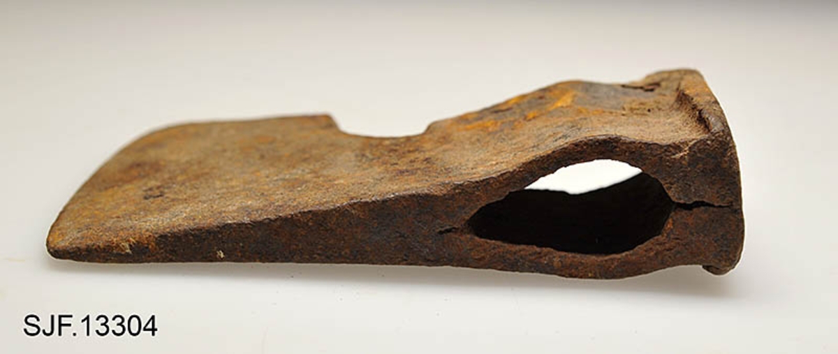 Økseblad uten skaft.  Redskapet er overført fra Borgarsyssel museum i Sarpsborg, dessverre uten proveniensinformasjon ut over at den skal være brukt i Østfold. 

Øksa er smidd, antakelig med innlagt stål i eggpartiet, men ettersom overflata er dekt av rust er det vanskelig å verifisere dette uten å foreta oppsliping.  Dette framstår som et forholdsvis tungt og bredt økseblad.  Med denne bladbredden har det neppe har vært beregnet på hogst, men det kan naturligvis ha vært brukt til barking, men også til ymse håndverksaktiviteter.  Den øvre delen (omkring øyet og nakken) er preget av slitasje.  Det nedenforliggende bladet er noe bredere.  Nakkedelen har opprinnelig vært flat og rektangulær, men den er brukt som hammer, noe som har ført til at godset er noe deformert og at det har dannet seg "skjegg" langs langsidene.  Øyet (skafthullet) har et dråpeformet tverrsnitt (cirka 5, 2 X 2, 6 centimeter). Godset mellom øyet og hammerflata på øksenakken er sprukket, noe som kan ha vært årsak til at redskapet ble kassert.  Eggdelen har betydelig større bredde enn nakkedelen. 