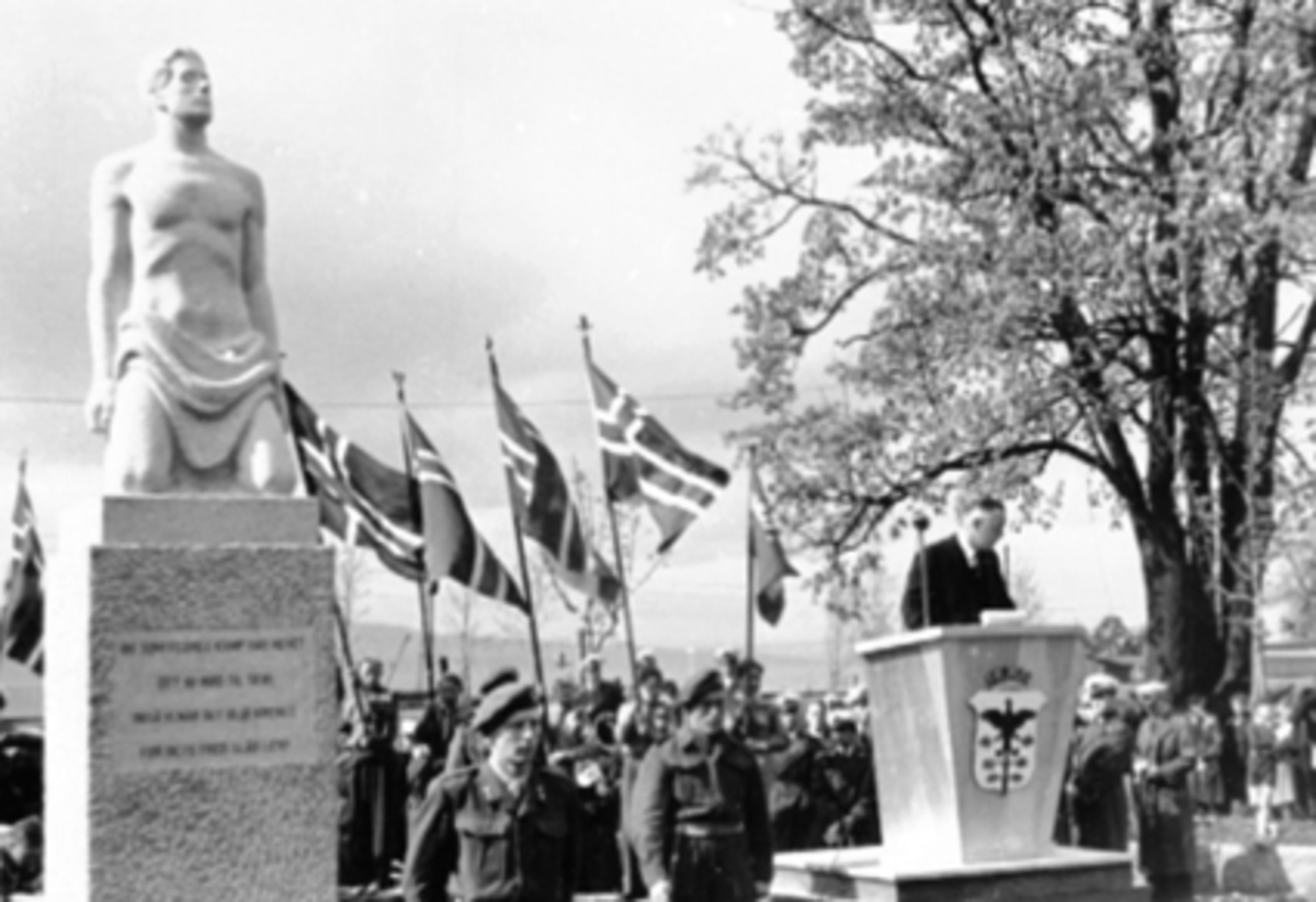 Postkort, Hamar, Strandgateparken, avduking av Minnesmerket over de falne, utført av Hamarkunstneren billedhugger Nils Flakstad, avduket 17. mai 1949, talerstol, æresvakter, flaggborg, talerstol med byvåpen, til minne om de 7 guttene fra Hamar som mistet livet under krigen, formann i minnesmerkekomiteen grosserer Sverre Nilssen informerte om arbeidet med bautaen og biskpp Schjelderup holdt avdukningstalen,