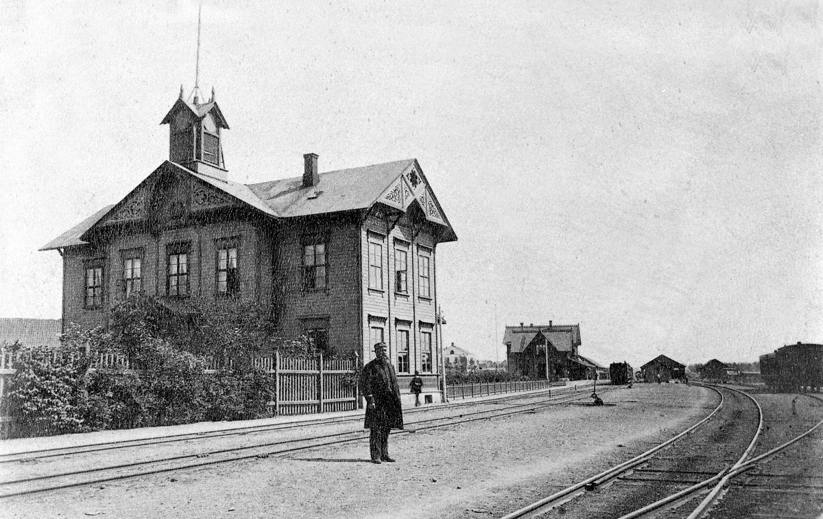 Hamar jernbanestasjon, NSB Norges Statsbaner, Hamars første stajonsbygning til venstre fra 1862, den andre stasjonsbygningen fra 1880 i bakgrunnen, stasjonsmester Christian Fredrik Lund (1883-1886) på perrongen