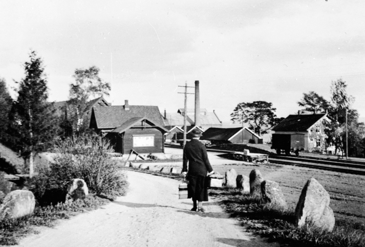 Ringskaer, Furnes, Jessnes, kvinne på veg ned til Jessnes stasjon, Jessnes Potetmelfabrikk i bakgrunnen.