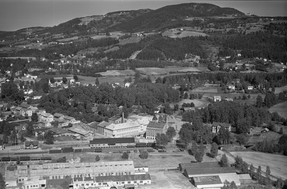 Flyfoto av Globus Maskinfabrikk, Brumunddal jernbanestasjon, potetmelfabrikken, Høyens Konfeksjonsfabrikk.