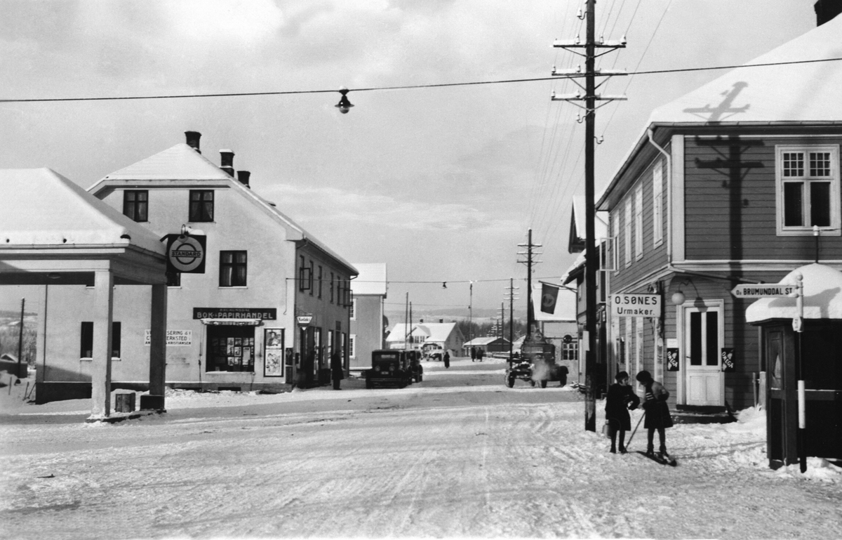 Furnesvegen, Brumunddal, vinter, jenter på ski, Standard bensinstasjon til venstre, Brumunddal Bok og Papirhandel, Brumundheimen kafe, urmaker Sønes til høyre.