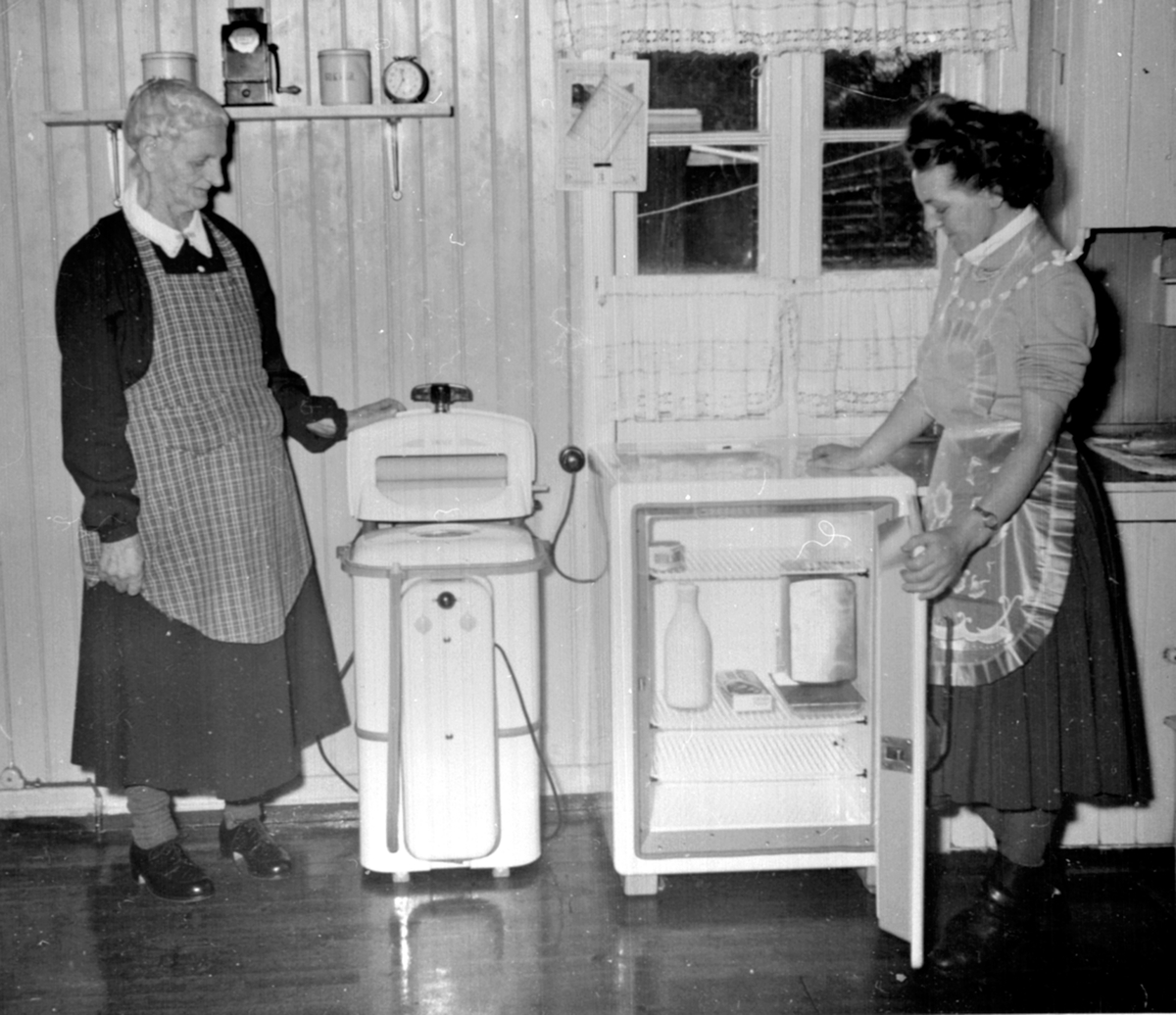 Interiør, kjøkken 2 damer med vaskemaskin og kjøleskap. Berger Langmoen A/S, Brumunddal. Høsten 1954 fikk alle ansatte på Langmoen 500 kroner for å kjøpe seg vaskemaskin. Til venstre er Petra Jevne og Paula Jevne g. Olsen.