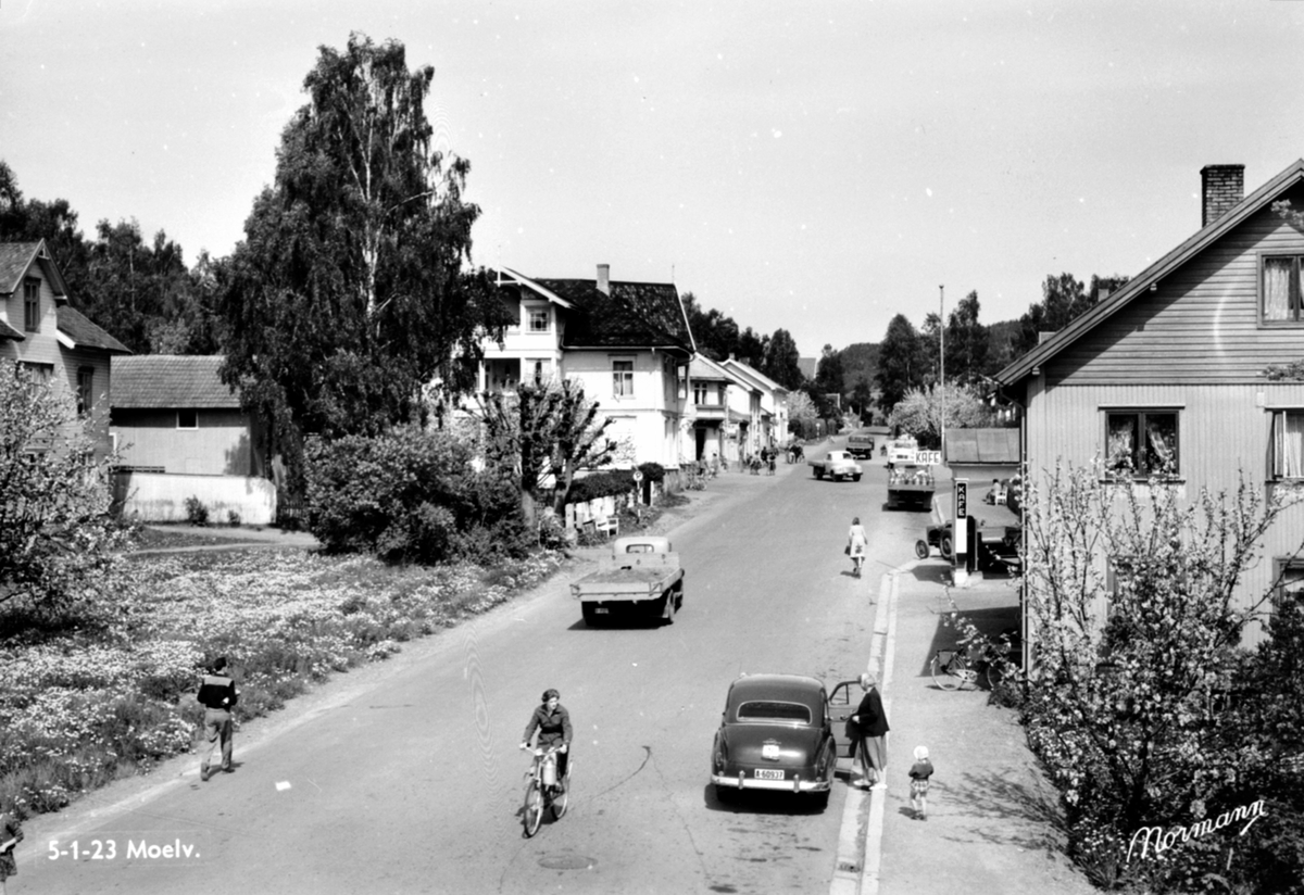 Postkort, Ringsaker, Moelv sentrum, Storgata med folk og biler, bil med registreringsnummer A-60397, til venstre: Storgata 114 M. P. Doblougs forretning, til høyre bensinstasjonen i Søberg i Storgata 113,