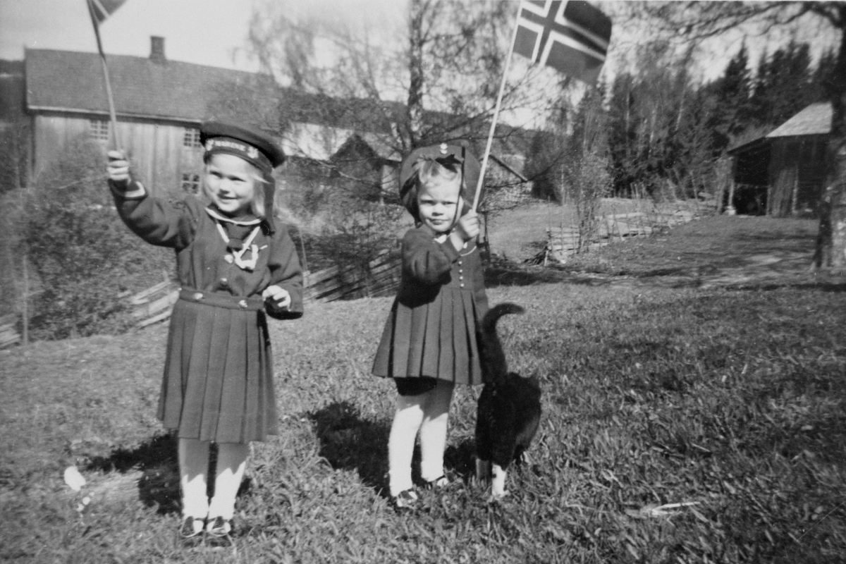 2 jenter med flagg og matroskjole, 17. mai. I bakgrunnen Gjerlaugbakken og Engelstad. May Gislaug Godager og Laila Oliv Godager.