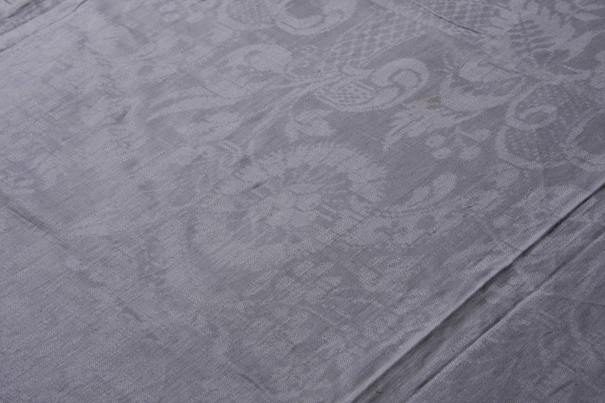 Hvit lindamask med mønster: damer til hest med jaktfalk, hornblåsende jegere med hunder, blomstermønster samt enkeltbord på langsidene. Smal fall på kortsidene. Merket med liten rød stjerne.