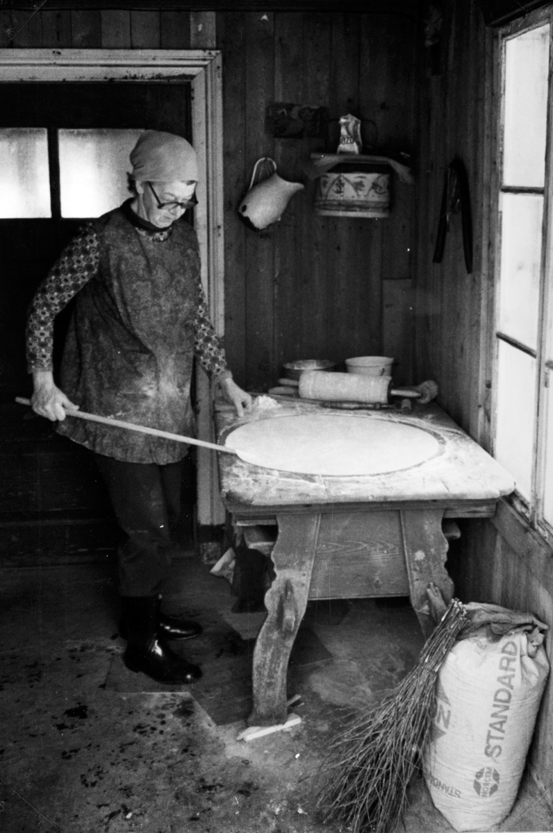 Lefsebaking i størhuset i Fossengen nordre, Vallset i desember 1978. Oline Rønningsbakken kjevler ut deigen på det gamle kjøkkenbordet fra 1800-tallet som engang ble plassert i dette rommet i størhuset. På veggen bak henger et gammelt lagget mjølkjrørel, gjort av Ole Syversen Fossengen 1847-1918. 