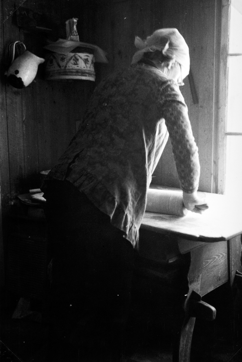 Lefsebaking i størhuset i Fossengen nordre, Vallset i desember 1978. Oline Rønningsbakken kjevler ut deigen på det gamle kjøkkenbordet fra 1800-tallet som engang ble plassert i dette rommet i størhuset. (Registrert av Oddmund Rønningsbakken)