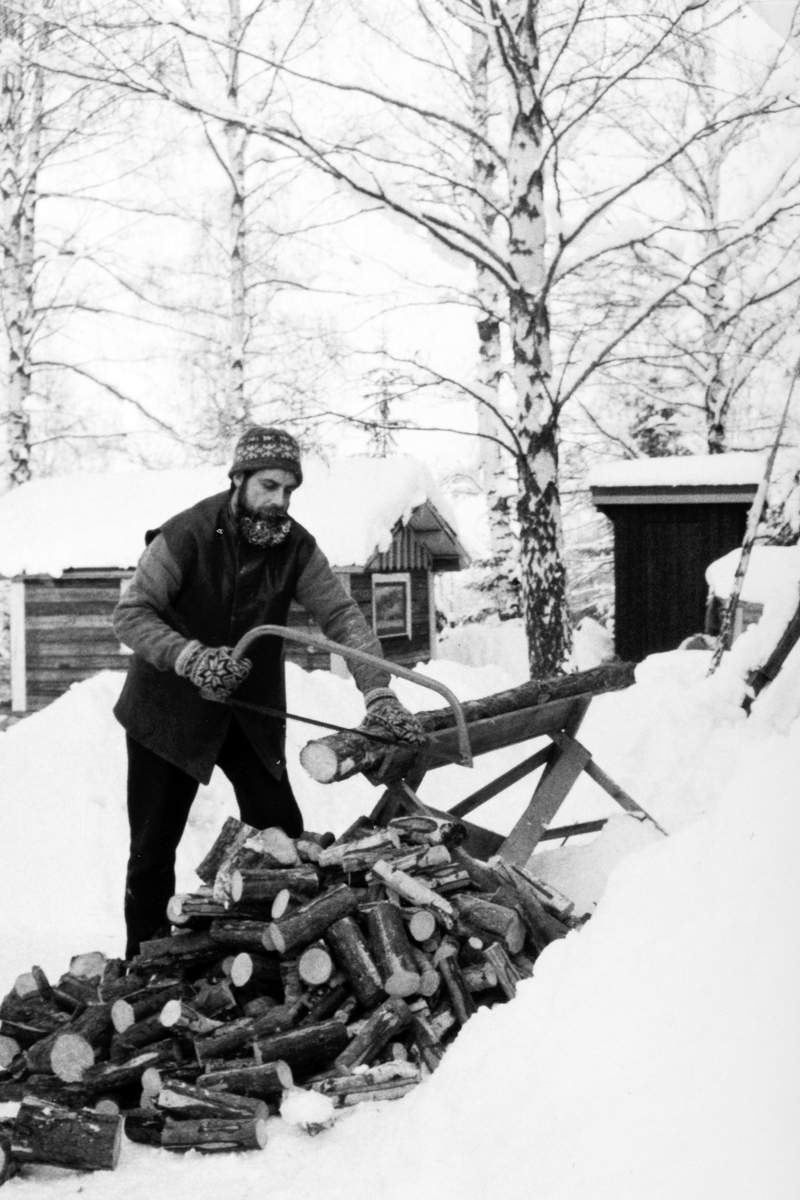 Oddmund Rønningsbakken sager ved en kald vinterdag vinteren 1978-79.. 
Sagkrakk, buesag. Rønningsbakken er iført vadmelsbukser, tjukk genser, foret skinnvest, god strikkelue og dobbelte ullvotter. Han saget mye ved på dene måten i mange år, både på 1970 og 1980-tallet. 