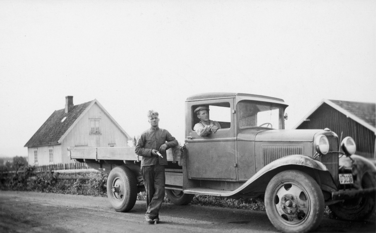 Ottar Myhre (1914-1973) stående utenfor lastebilen. Og Olaf Nerhagen (1915-1974) sittende inne i bilen. I bakgrunn sees Hagen ved Hverven i Ottestad. Bilde er tatt av Lenhart Nerhagen, som også er bil eieren. Bilde er tatt i 1937. 
