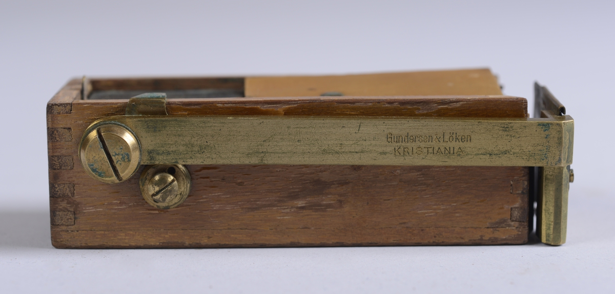 Måleinstrument oppbevart i rektangulært etui av skinn. Etuiet har reim og metallspenne for feste av lokket på front, og hemper på sidene.

Selve treesken:  10*3*4 cm.  Lengde på messingdelen:  10 cm.  Bredde på messingdelen:  1 cm.  Messingskiva fremme:  3*3 cm.  Etuiet:  6*10,5*4 cm.  Etui-lokket:  4,5*5,5*6,5 cm.
