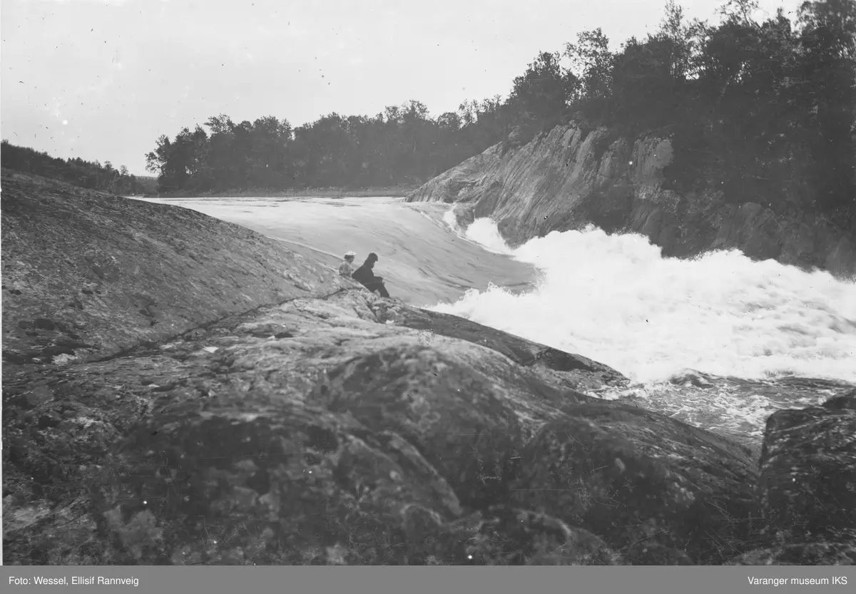Harefoss i Pasvik. Et par sitter ved elvekanten og ser utover fossen.