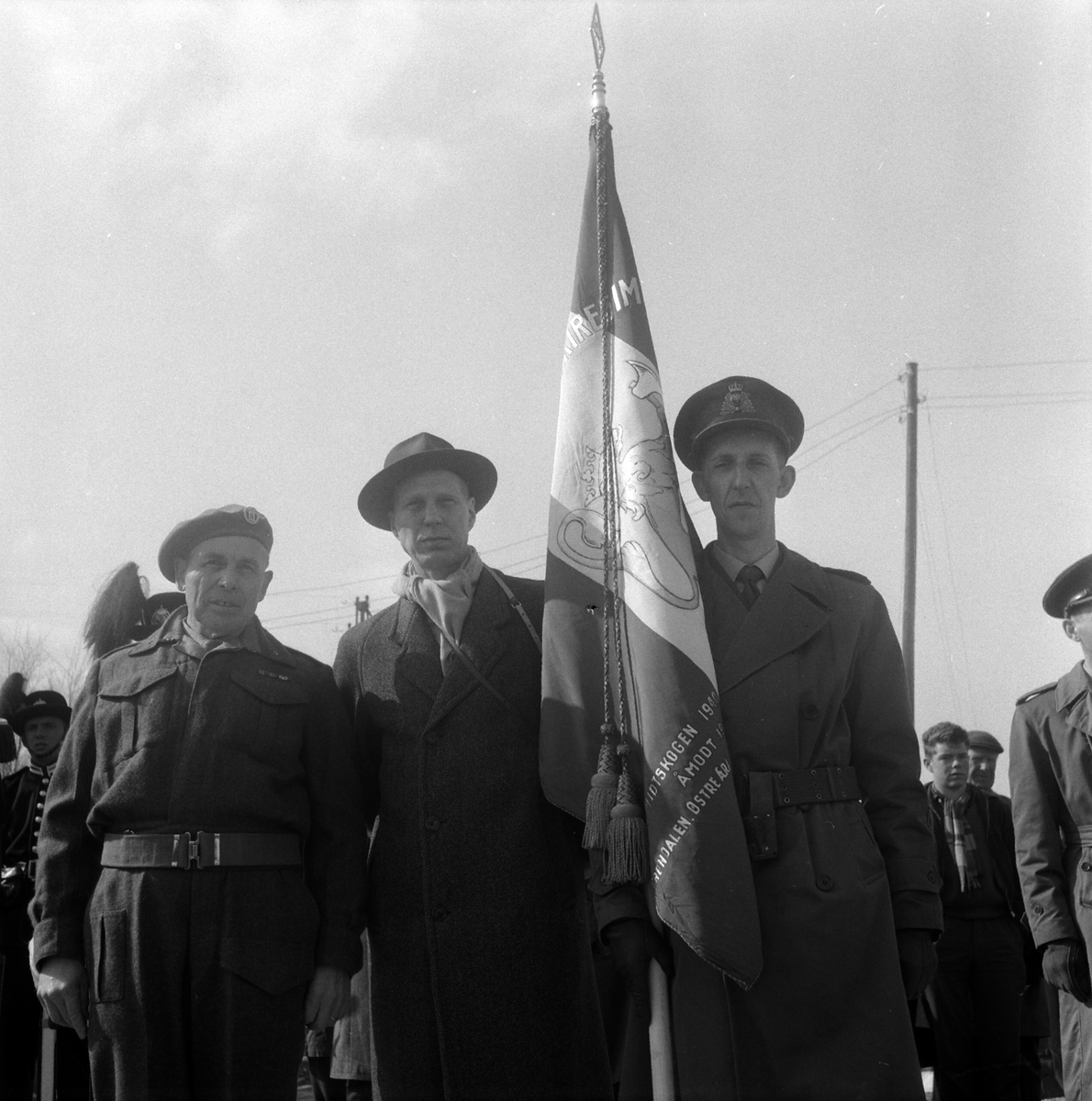 Elverum, Midtskogen, kong Olav og kronpris Harald ved avdukingen av krigsminnesmerke over trefninger med tyske styrker under andre verdenskrig 9. april 1940, " Må denne sten minne om offervilje og innsatsvilje for Norge" sa kong Olav 9. april 1960 foran 4000 tilskuere, tre ukjent menn med fane, 
(antatt ?: fenrik Halvor Mørk til venstre og fenrik Odd Øien til høyre som deltok i krigshandlingene)