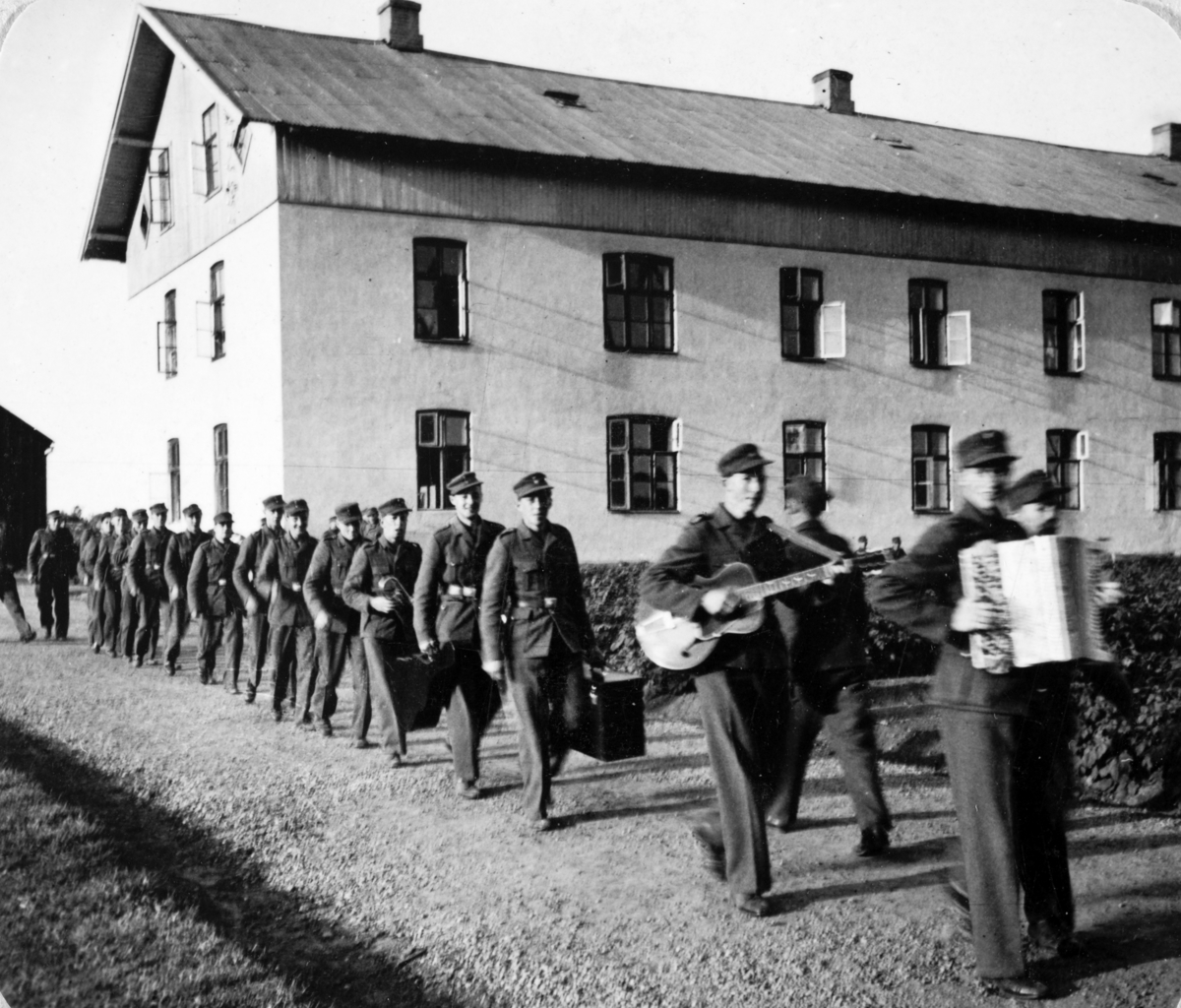 AT-tjeneste på Ådalsbruk i Løten, 26. august 1942 til 26. november 1942. Arbeidsdistrikt nr. 1. Arbiedsfylking IV. Sveit nr. 5. Forleggingssted Ådalsbruk. Arbeidstjenesten under 2. verdenskrig. "Orkesteret med håndlangere, kor og dirigent på utmarsj". Kaserna, Murgården i bakgrunnen. 
Se artikkel i Lautin, årbok for Løten 1993. 