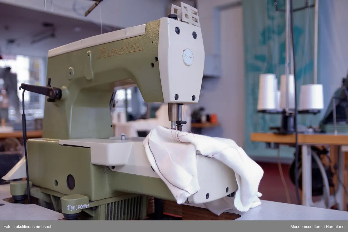 Rimoldi-symaskin montert på lite bord med pedalar og motor under bordet, og stativ til to trådsneller og trådførarar ved sidan av maskina. Strømbrytar er plassert under bordet.

Motor: Etka Variostop
Typ: VD 12
Nr. 08315789
3~Mot (triangel)Y 220/380 V
2,6 / 1,5 A     550 W
2800 / 3400 1/min
...
Made in Western Germany