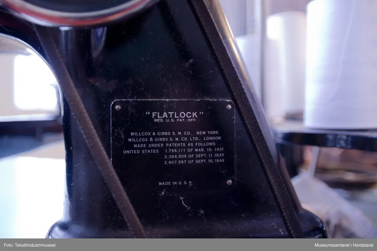 Flatlock-symaskin i svartmåla støypejern og med halvautomatisk oljing. Maskina er montert på eit Juc-bord og har Singer-motor (truleg ikkje original).

Motor: Singer alternating current electric transmitter. No. K 692357 R
Volts: 210-230.