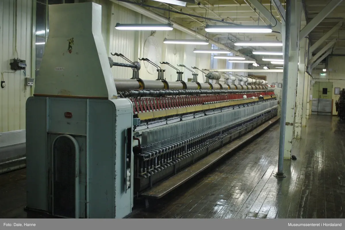 Elektrisk ringspinnemaskin (1958) frå det sveitsiske selskapet Rieter. Øvst på maskina plasserer ein spolane med forgarn frå kardemaskina. Reint teknisk er det tre hovudelement i spinninga:  forgarnet blir strukke, tvista (snodd) for å få meir styrke, før det ferdige garnet blir oppvikla på ein spole eller 'spinnepipe'. Tråden går under eit transporthjul i tre, gjennom støypte løpegangar og vidare nedover: Garnet blir snodd ved at garnet passerer ein løpar som beveger seg på ein ring, før det blir samla på ein sylindrisk metallspole. Det er ei rekkje små støvsugarar langs heile maskina, små røyr som stikk ut over spolane. Desse syg til seg støv og/eller tråden viss den ryk, for å unngå at den kjem inn i maskina. Trådrestar og støv blir samla opp i eit oppsamlingskammer på venstre sida av maskina. Der er det òg ein målar som måler kor mykje maskina spinner.

Drivverket og ein stjernemotor sit på høgre sida av maskina. På sida står det "Rieter" i raudt, og det er to målarar som måler omdreiingar/hastigheit på maskina. Det er ei rekkje med 136 koner på kvar side. Maskina kan byggjast på i seksjonar, og slik utvidast etter behov, noko som er vanleg for spinne- og spolemaskiner.