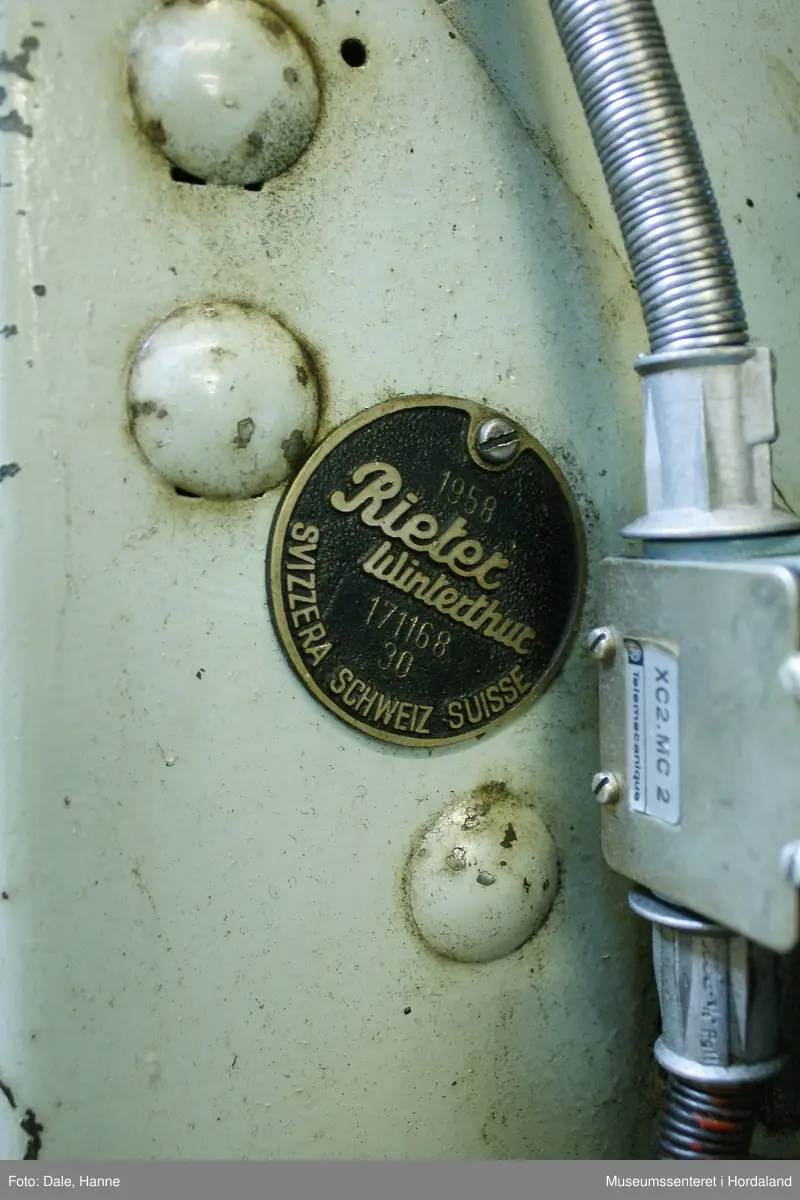 Elektrisk ringspinnemaskin (1958) frå det sveitsiske selskapet Rieter. Øvst på maskina plasserer ein spolane med forgarn frå kardemaskina. Reint teknisk er det tre hovudelement i spinninga:  forgarnet blir strukke, tvista (snodd) for å få meir styrke, før det ferdige garnet blir oppvikla på ein spole eller 'spinnepipe'. Tråden går under eit transporthjul i tre, gjennom støypte løpegangar og vidare nedover: Garnet blir snodd ved at garnet passerer ein løpar som beveger seg på ein ring, før det blir samla på ein sylindrisk metallspole. Det er ei rekkje små støvsugarar langs heile maskina, små røyr som stikk ut over spolane. Desse syg til seg støv og/eller tråden viss den ryk, for å unngå at den kjem inn i maskina. Trådrestar og støv blir samla opp i eit oppsamlingskammer på venstre sida av maskina. Der er det òg ein målar som måler kor mykje maskina spinner.

Drivverket og ein stjernemotor sit på høgre sida av maskina. På sida står det "Rieter" i raudt, og det er to målarar som måler omdreiingar/hastigheit på maskina. Det er ei rekkje med 136 koner på kvar side. Maskina kan byggjast på i seksjonar, og slik utvidast etter behov, noko som er vanleg for spinne- og spolemaskiner.