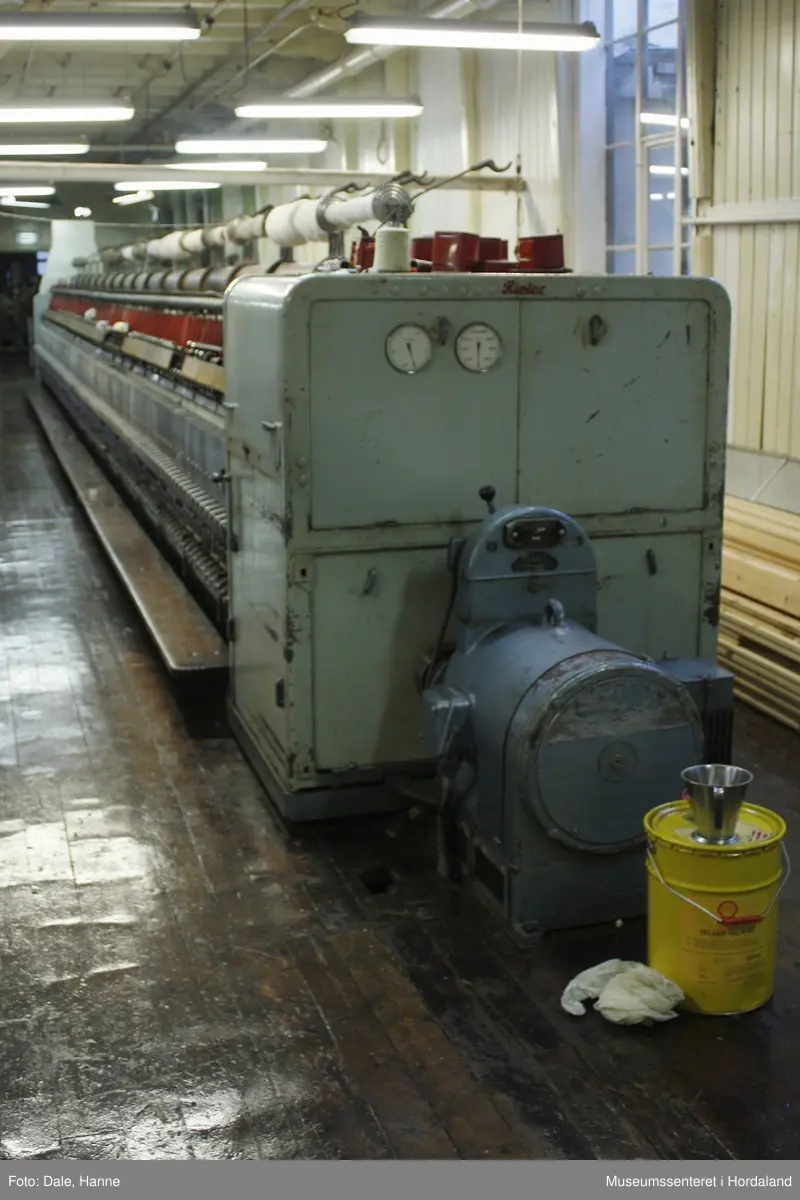 Elektrisk ringspinnemaskin (1958) frå det sveitsiske selskapet Rieter. Øvst på maskina plasserer ein spolane med forgarn frå kardemaskina. Reint teknisk er det tre hovudelement i spinninga:  forgarnet blir strukke, tvista (snodd) for å få meir styrke, før det ferdige garnet blir oppvikla på ein spole eller 'spinnepipe'. Tråden går under eit transporthjul i tre, gjennom støypte løpegangar og vidare nedover: Garnet blir snodd ved at garnet passerer ein løpar som beveger seg på ein ring, før det blir samla på ein sylindrisk metallspole. Det er ei rekkje små støvsugarar langs heile maskina, små røyr som stikk ut over spolane. Desse syg til seg støv og/eller tråden viss den ryk, for å unngå at den kjem inn i maskina. Trådrestar og støv blir samla opp i eit oppsamlingskammer på venstre sida av maskina. Der er det òg ein målar som måler kor mykje maskina spinner.

Drivverket og ein stjernemotor sit på høgre sida av maskina. På sida står det "Rieter" i raudt, og det er to målarar som måler omdreiingar/hastigheit på maskina. Det er ei rekkje med 136 koner på kvar side. Maskina kan byggjast på i seksjonar, og slik utvidast etter behov, noko som er vanleg for spinne- og spolemaskiner.