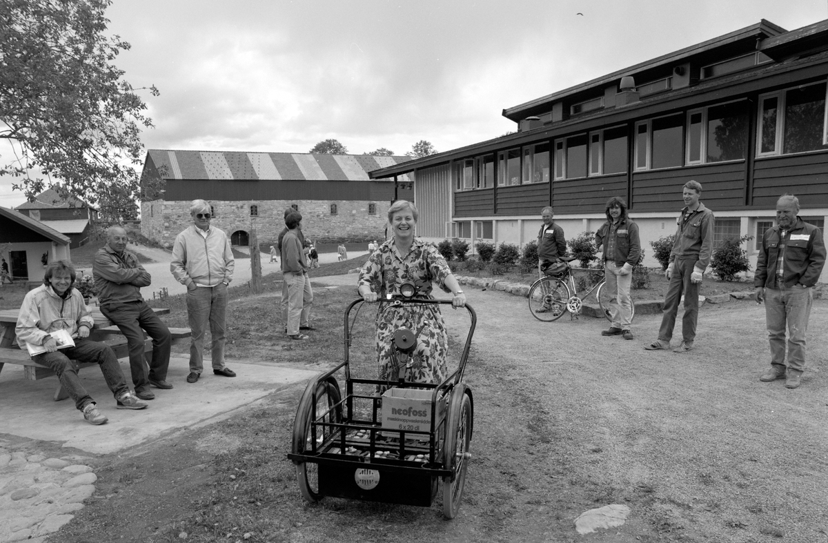 Gruppe ansatte ved Hedmarksmuseet ved restauranten, mot Storhamarlåven. Wenke Melbye sitter på en elektrisk varesykkel, konstruert av ingeniør Sverre Hagen, fra 1920-30 tallet. "Ing. Hagens elektro-varesykkel." Sannsynligvis produsert ved "Norsk Elektrodrift" i Brumunddal.