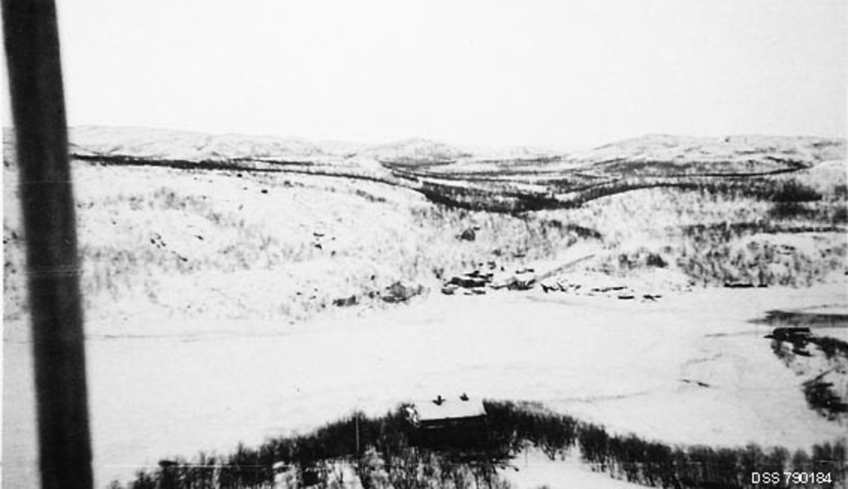 Utsikt mot Elvenes i Sør-Varanger i Finnmark.  Bildet er tatt en vinterdag.  Fotografen har antakelig stått på høgdedraget Trifonhøgda med kameraetn vendt mot den innerste delen av Bøkfjoden og Pasvikelvas utløp i denne fjorden ved Elvenes.  Der skimter vi en del bebyggelse ved strandsonen.  Ellers var landskapet preget av kvite snø- og isdekte flater med strimer av skog, i stor utstrekning bjørkeskog.