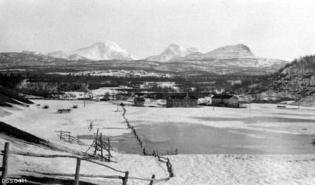 Snødekt kulturlandskap i Målselv i Troms.  Fotografiet er tatt fra en bakkekam ned mot flate.  På denne flata stikker et gjerde opp av snøen, og til venstre for gjerdet skimtes også hesjer med rajer til å legge gras på for høytørk.  Disse ble antakelig gjenbrukt år etter år.  I motsatt ende av denne flata ser vi tunet på eiendommen Søndre Olsborg, som etter hvert ble bosted for statens skogforvalter i Troms forvaltningsdistrikt.  Sentralt i tunet ligger et halvannenetasjes våningshus, oppført i sinlaft og merd en ark sentralt på den sida av taket som vender mot de omkringliggende åkerarealene.  Til høyre for våningshuset ligger en driftsbygning, tilsynelatende oppført med laftevegger i førsteetasje og med skjelterverk eller bordkledd bindingverk i overetasjen.  Til venstre for våninghuset en noe mindre bygning, muligens et stabbur.  Bakenfor gardstunet ser vi moer med skog, og mot horisonten rager høye, skogbare fjell. 

Gardsenheten Søndre Olsborg ble til etter at Reier Amundsen Olsborg delte og solgte garden sin til ulike etterkommere i begynnelsen av 1890-åra.  Denne gardparten var det sønnen Ole Reisersen som fikk hand om.  Han giftet seg i 1898 med enka Berte Pauline Petersdatter fra Malangen, i de fikk en sønn i 1901. Ole Reiersen død da gutten var fem år gammel.  Etter denne hendelsen ble eiendommen først skjøtet over på den mindreårige sønnen, som forvaltet verdiene med bistand fra en verge.  I 1910 ble utfordringene forsøkt løst ved opprettelse av ei forpaktningskontrakt med skogforvalter Sakshaug, som forpliktet seg til å drive og vedlikeholde eiendommen mot en godtgjørelse til den unge eieren i minst fem år.  Det er sannsynlig at dette dokumentet bekreftet en allerede eksisterende relasjon.  Høsten 1910 kjøpte i Anders Sakshaug Søndre Olsborg for 4 000 kroner.  Han lånte en stor del av det nevnte pengbeløpet av svigerfaren, som var gardbruker i Drøbak.  Ved kongelig resolusjon av 7. juni 1916 ble det bestemt at staten skulle kjøpe eiendommen Søndre Olsborg som skogforvalterbolig.  Med i handelen fulgte, foruten jordvegen og gardstunet, rettigheter til et sag- og møllebruk.  Bakgrunnen for denne transaksjonen må ha vært at Anders Sakshaug sommeren 1916 fikk ny stilling som skogforvalter i Valdres og flyttet dit, og at det statlige skogvesenet trengte en embetsbolig for etterfølgeren Arthur Solemslie og hans kone Ruth, som kom flyttende nordover til en for dem ukjent region. 

Noen dokumenter som viser bakgrunnen for at Søndre Olsborg ble skogforvalterbolig finnes under fanen «Opplysninger». 