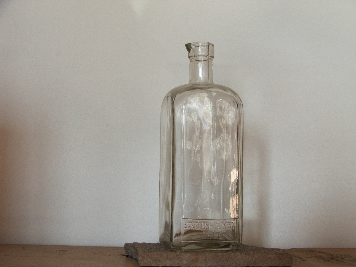 En firkantet blank flaske med helletut.Firmanavnet står på den ene siden.