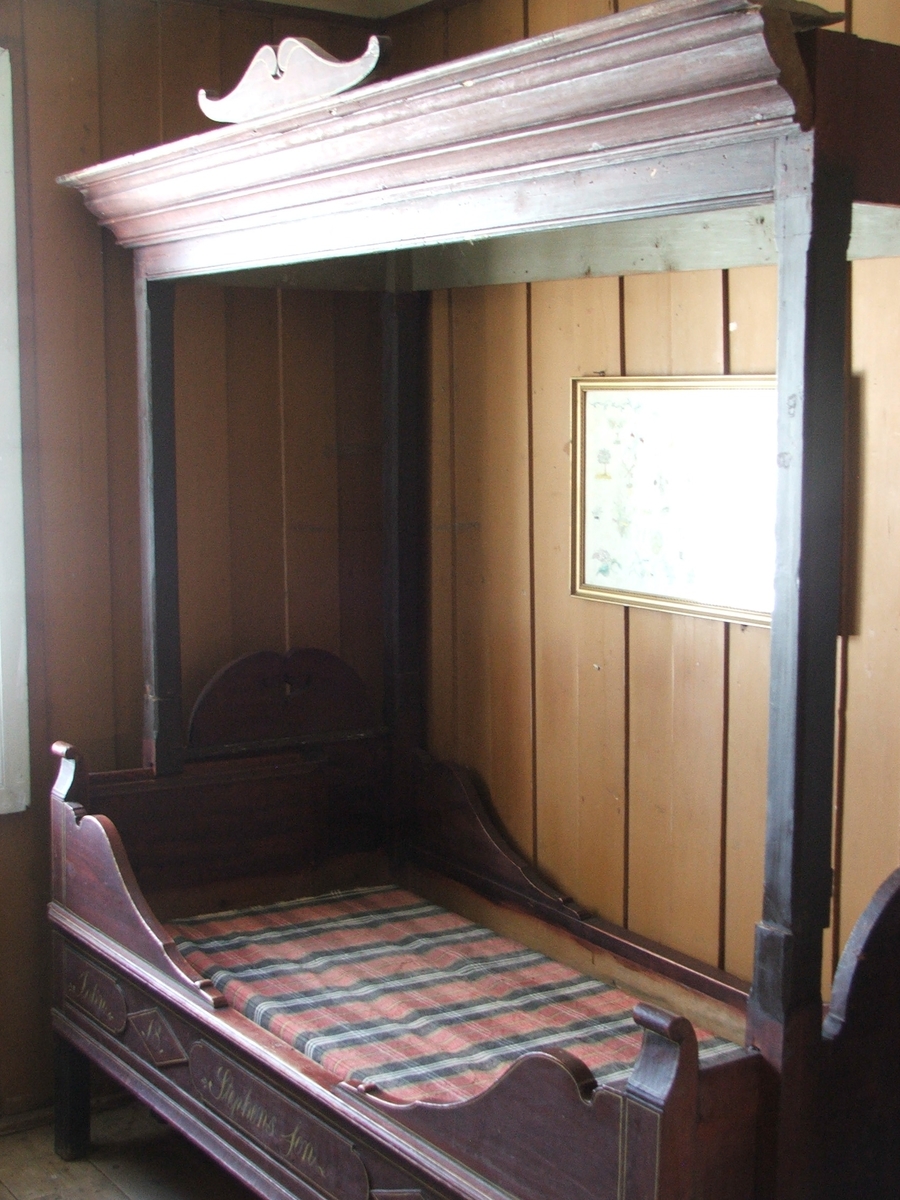 En skuvseng med 4 sengestolper og himling, utskjæringer ved sengevangene og øverst. Mangler forheng. Inskripsjon malt i gult foran. Himlingen er festa med tapper på sengestolpene.